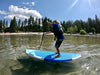 Young boy paddleboarding on lake tahoe with crystal clear water, blue skies with beautiful white clouds and bright green trees in the background.  Boy on a waterkids 7'6ft kids surf sup paddleboard that is get for in the ocean surfing waves as well as paddling on the lake