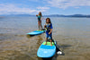 2 kids a young boy and youth age girl paddling towards the camera on the 8ft waterkids explorer soft top kids paddle boards.  Lake Tahoe on a non busy day with adults and children playing in the water and beautiful mountains behind them.  Both kids are paddling with high smiles having a great time showing how good the kids boards are.