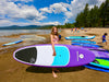 Young girl about 12 years old holding her paddle board on her own showing how easy it is to carry her lightweight waterkids 8ft girls paddleboard on her own without any help from an adult.  She is on the beach with lots of other kids who are playing and having a fun summer day at lake Tahoe