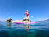 Cute Shot of a girl in a pink outfit paddling her purple color paddle board across an amazing emerald crystal clear blue water picture of lake Tahoe California.  She is paddling from right to left with granite white rocks in the water behind her, amazing mountain views and stunning free and blue water.  She is on her waterkids 8ft lotus paddle board for girls
