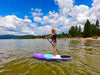 Amazing picture of a girl on her purple colored paddle board at lake tahoe california.  Beautiful scene with calm emerald color water, and beach with a wood pier in the background as well as spectacular mountain views with bright green trews blue skies and puffy white clouds.  Girl about 11 years old on her waterkids 8ft lotus sup for kids