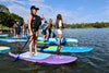 Group of kids at sup camp on their waterkids stand up paddle boards.  Girl in the front on her purple lotus 8ft paddleboard with hat on smiling looking towards where she will be paddling.  Kids in the background paddling and having a good day getting ready to learn water sports.  