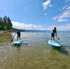 2 youth boys age 9 or 10 and 11 or 12 on their kids size paddle boards paddling on lake Tahoe California.  Boys paddle on a clear emerald blue lake with trees, mountains and blue skies.  Waterkids maui paddle board surf sup for kids  