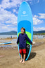 Young boy about 9 or 10 years old in the trophy pose holding his paddle board vertically behind him with a hug smile for victory. Kids soft top sup paddleboard the waterkids 8ft explorer soft top that is for youth paddlers.  Lake background with children paying in the lake and having a great time on a summer day with a beautiful mountain view behind them