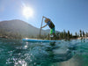 9'6 Kids Paddle Board Tahoe SUP for children and youth size paddlers.  Young paddle boarder paddling from right to left on a sunny day at lake tahoe with clear water and mountains in the background and wearing a straw hat for protection from the sun and a life jacket for safety