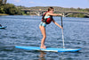 Youth aged girl about 9 or 10 years old paddleboard on a blue board with a striped traction pad and a sup white paddle. Girl is on the 7'6 Maui Kids Paddle Board SUP with a bridge in the background and she is paddling from left to right