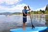 Youth paddler with a huge smile on his brand new waterkids 9'6 surf sup as lake tahoe.  Standing on his board with his carbon fiber adult size paddle that has a blue wave logo on the blade.  Kids on his paddle board on the lake with a pier and mountains and jet skis ion the background